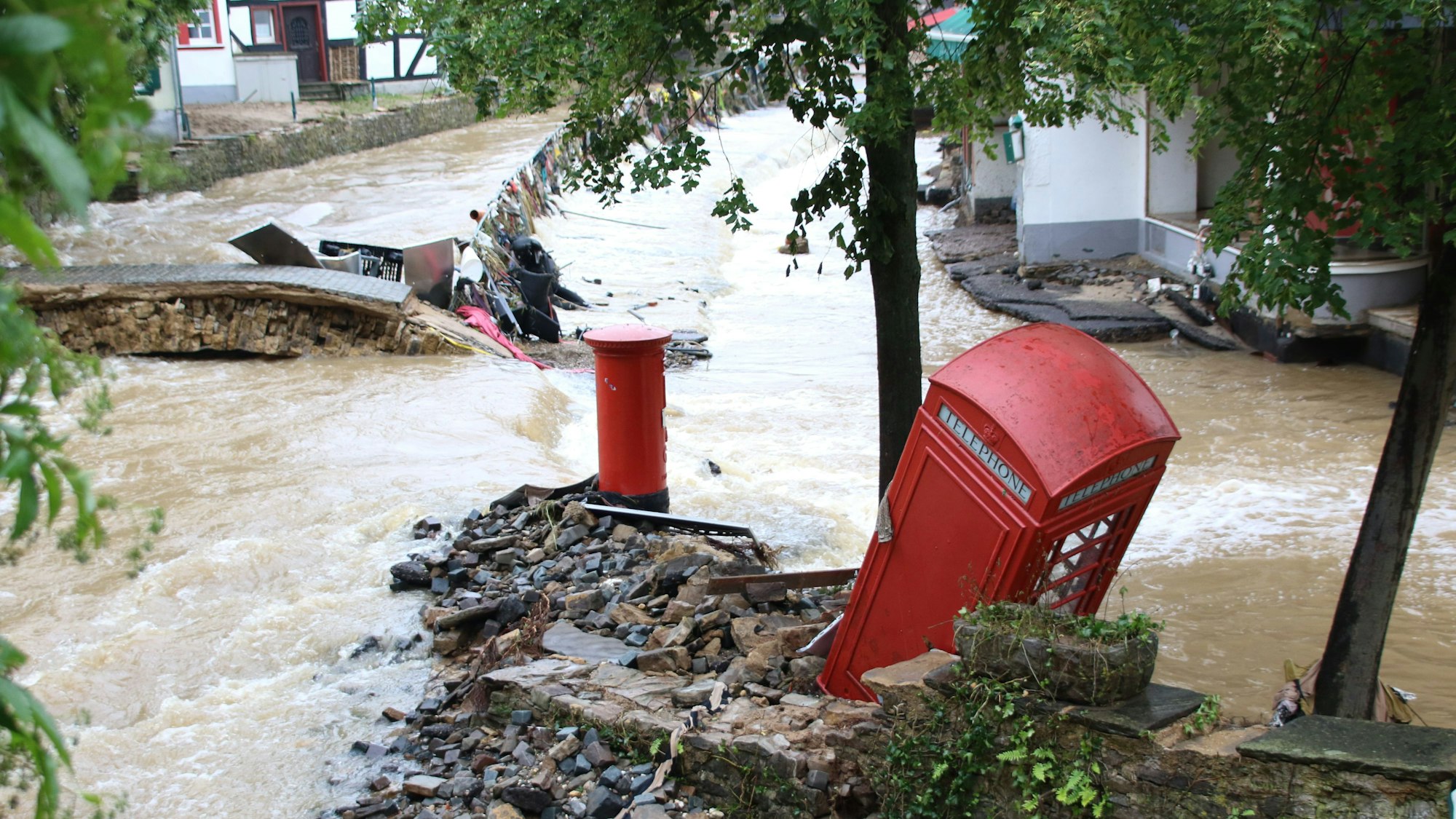 Ein Foto der Flutkatastrophe 2021: Bad Münstereifel ist überschwemmt, eine rote Telefonzelle, die als Bücherschrank genutzt wurde, steht umgeknickt auf einer Insel. Im Hintergrund ist eine zerstörte Brücke zu sehen.