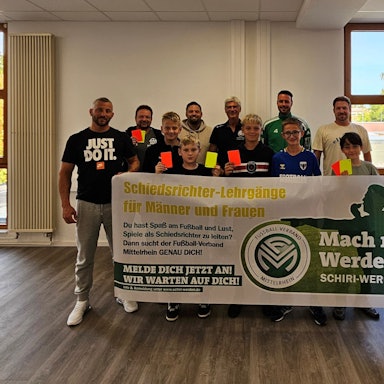 Die elf neuen Schiedsrichter und der Vorsitzende des Schiedsrichterausschuss halten Gelbe und Rote Karten ins Bild und ein Werbebanner für das Schiedsrichterwesen hoch.