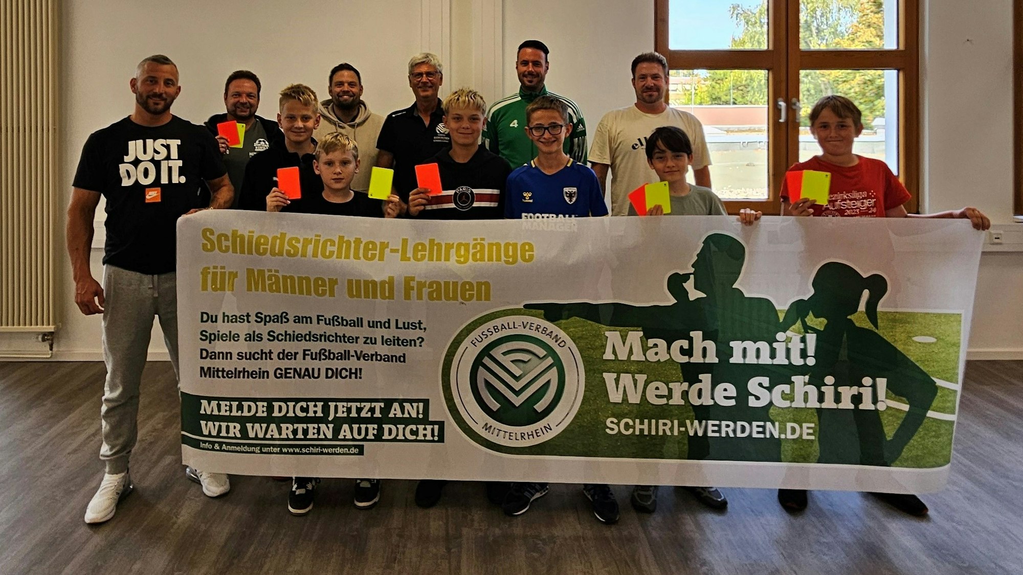 Die elf neuen Schiedsrichter und der Vorsitzende des Schiedsrichterausschuss halten Gelbe und Rote Karten ins Bild und ein Werbebanner für das Schiedsrichterwesen hoch.