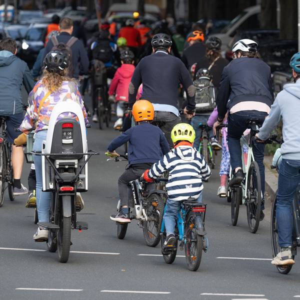 In einem Konvoi fahren Kinder und Erwachsene auf ihren Fahrrädern durch eine Stadt.