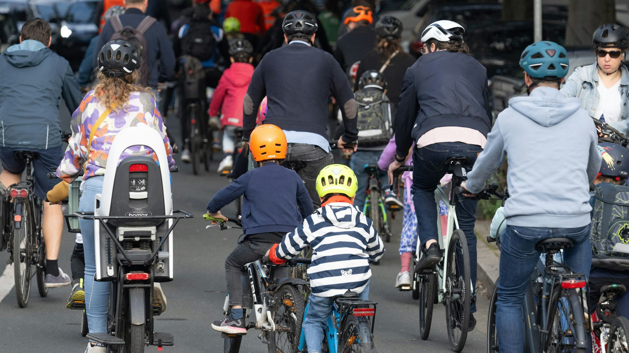 In einem Konvoi fahren Kinder und Erwachsene auf ihren Fahrrädern durch eine Stadt.