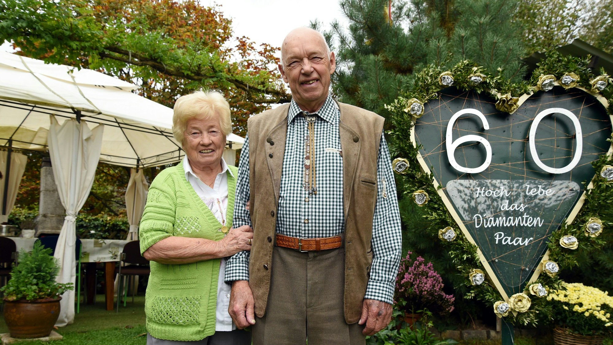 Katharina und Werner Hagen stehen auf einer Feier nebeneinander. Neben ihnen ist ein geschmücktes Herz zu sehen, mit einer silbernen 60. Darin stet: „Hoch lebe das Diamanten Paar“
