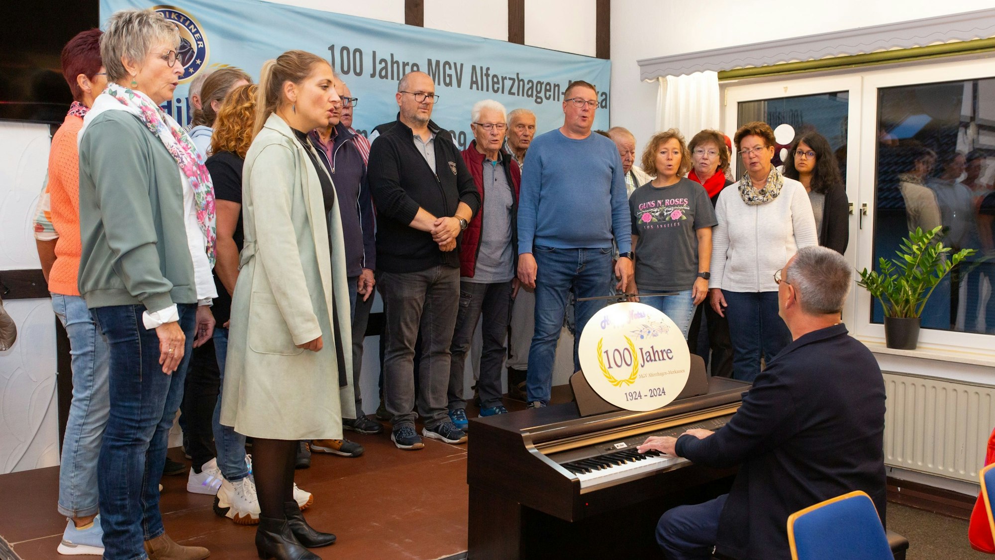 Ein Chor probt auf der Bühne, davor der Chorleiter am Klavier.
