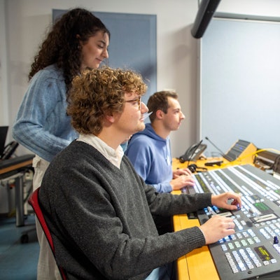 Zwei junge Männer und eine Frau arbeiten an einem Regiepult.