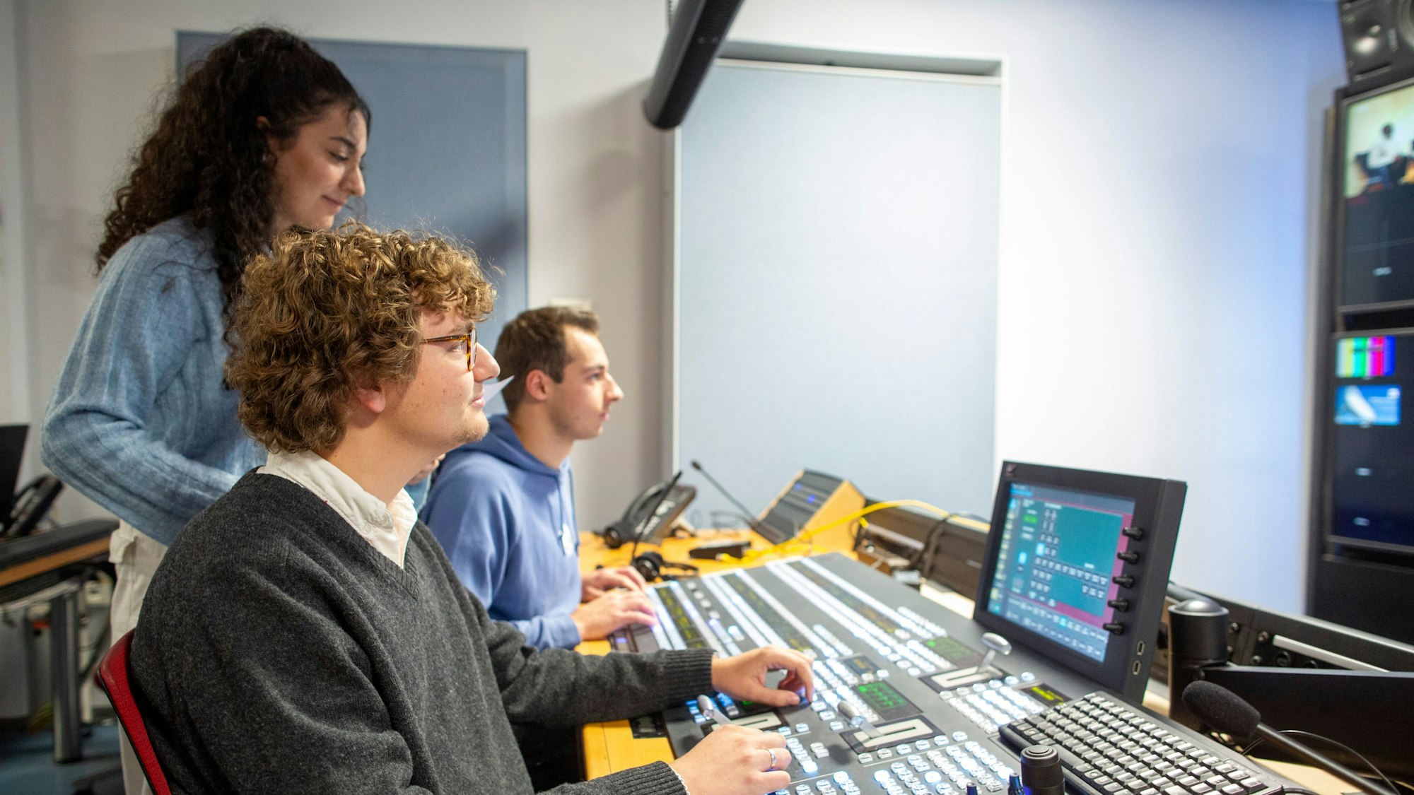 Zwei junge Männer und eine Frau arbeiten an einem Regiepult.