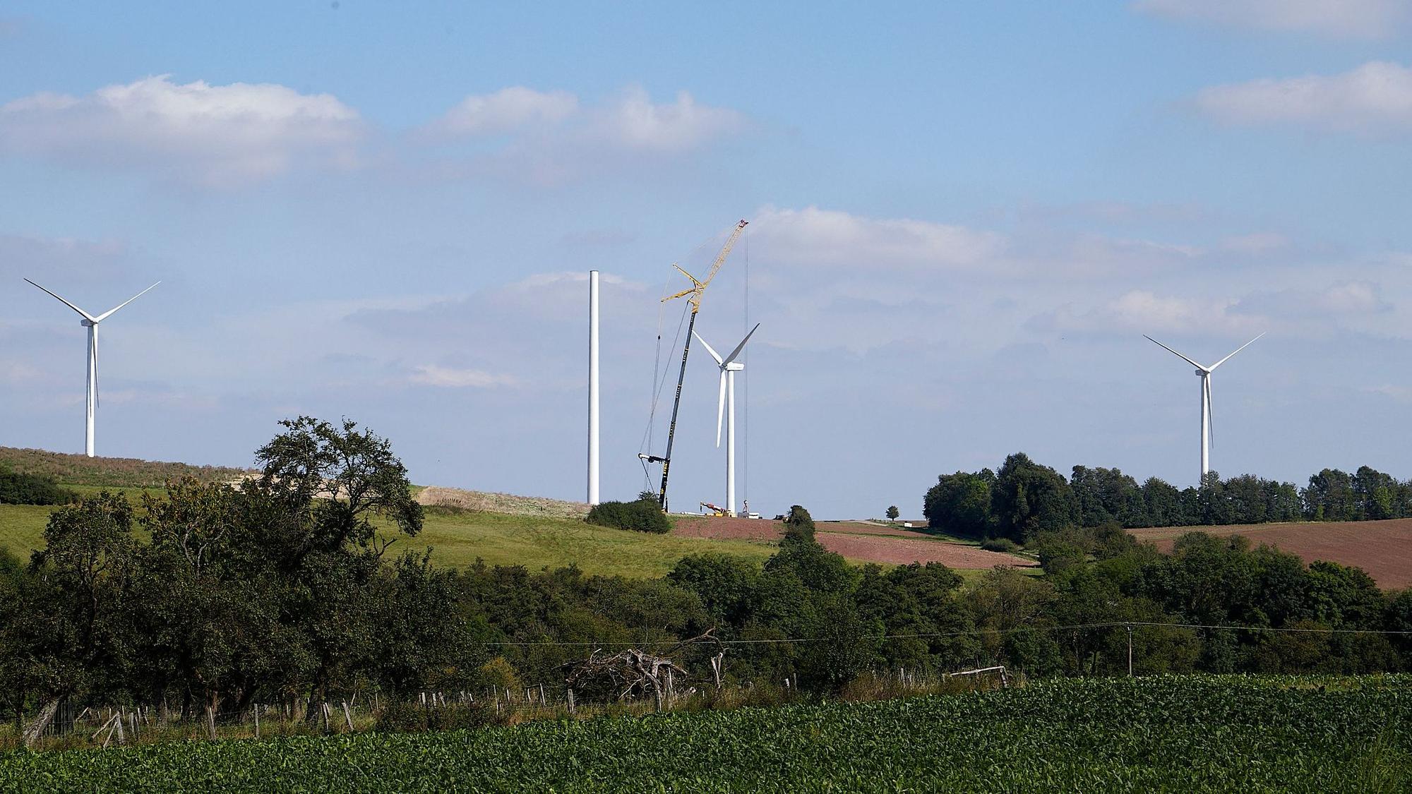 Auf einem Hügel bei Heimbach-Vlatten sind drei Windenergieanlagen zu sehen. Von einer vierten steht der Turm, mithilfe eines Krans wird daran gearbeitet.