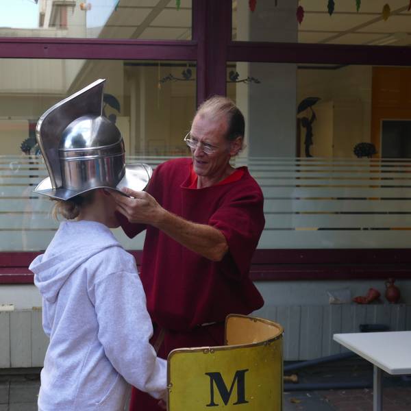 Ein Mann setzt einem Mädchen einen römischen Gladiatorenhelm auf den Kopf.