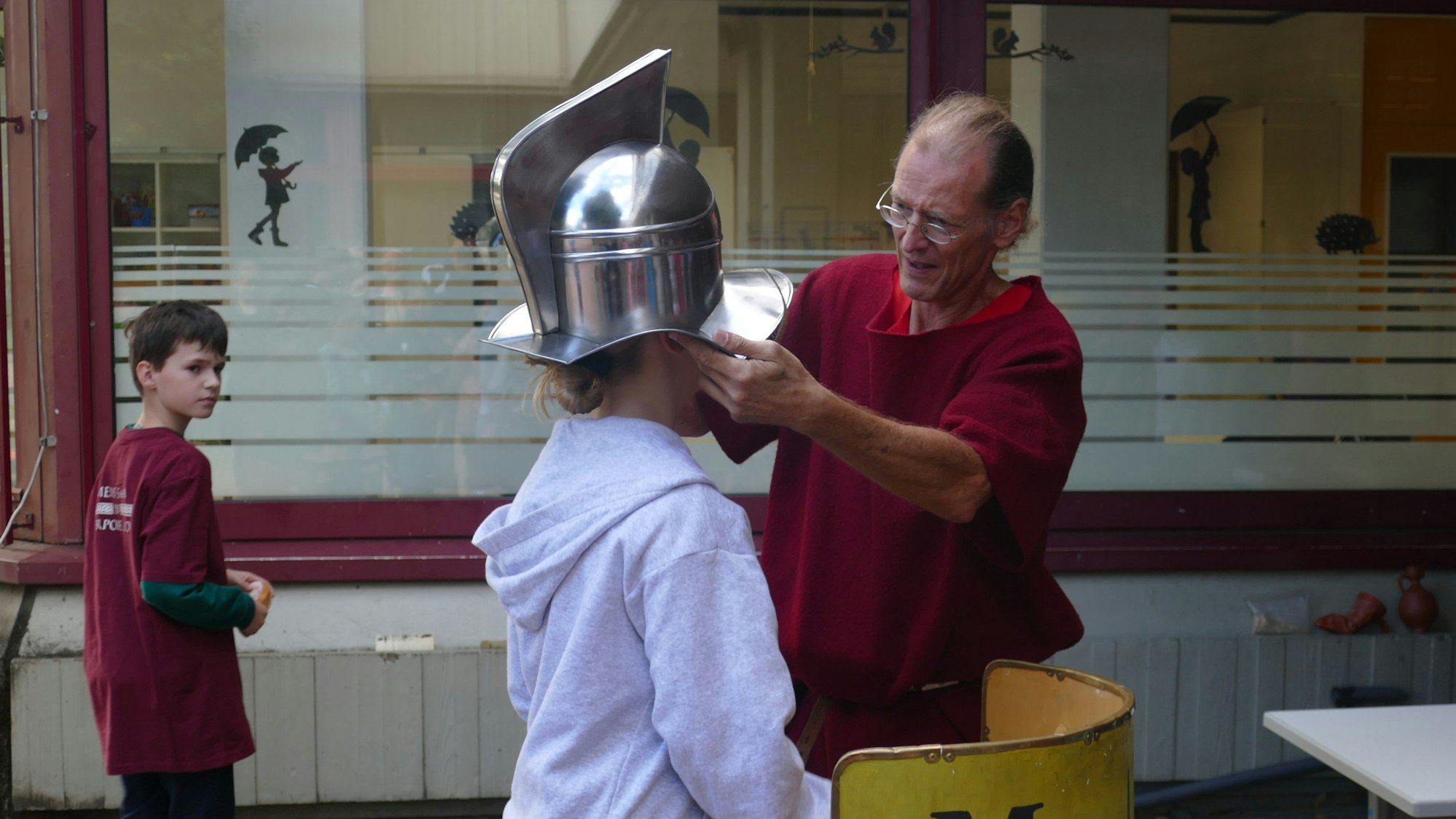 Ein Mann setzt einem Mädchen einen römischen Gladiatorenhelm auf den Kopf.