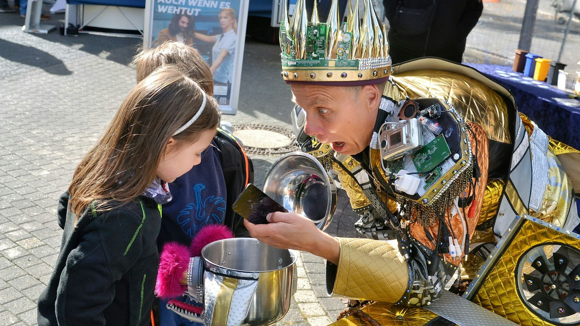 Das Bild zeigt einen Mann, der ein Smartphone aus einem Kochtopf geholt hat und es zwei Kindern präsentiert.