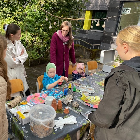 Kinder basteln an einem Tisch, dahinter stehen junge Frauen.