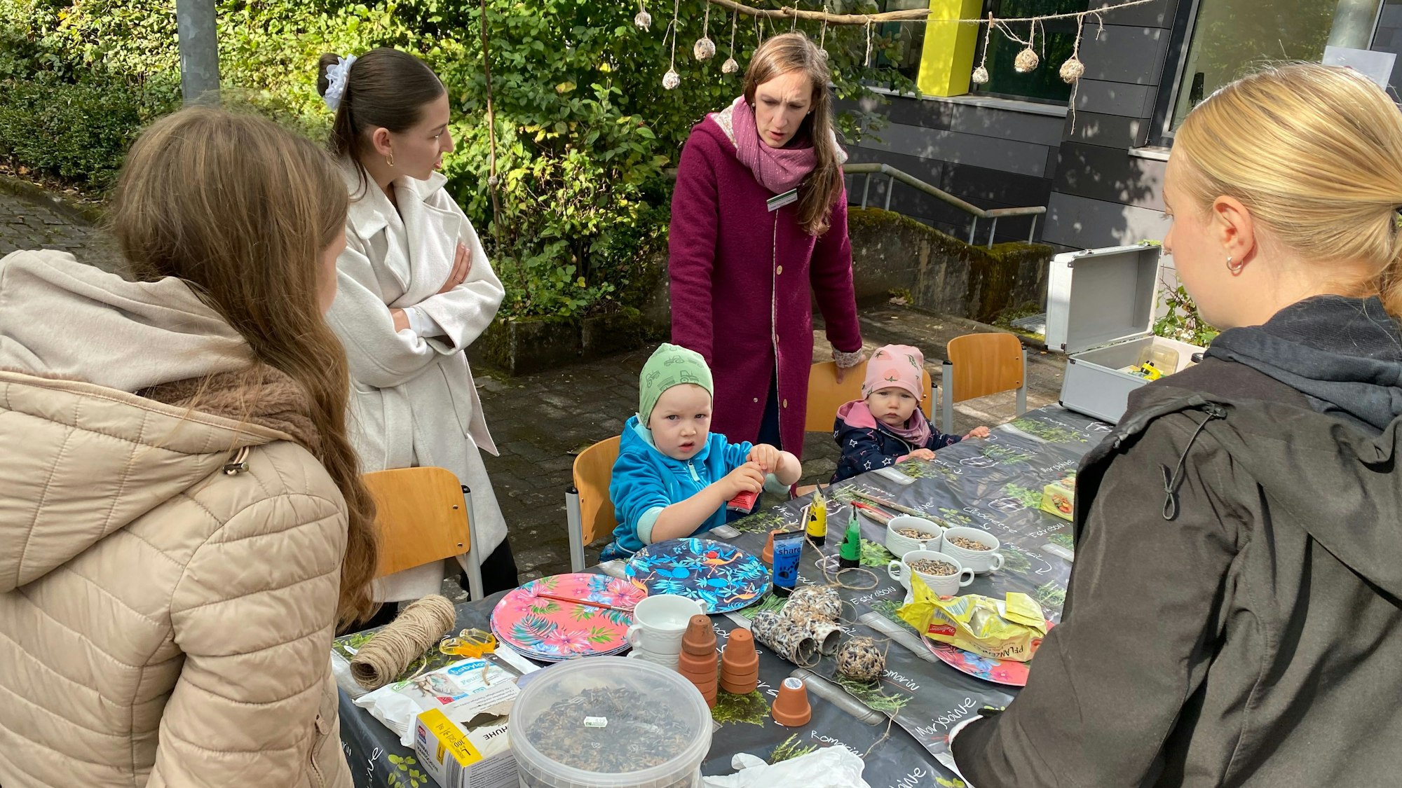 Kinder basteln an einem Tisch, dahinter stehen junge Frauen.