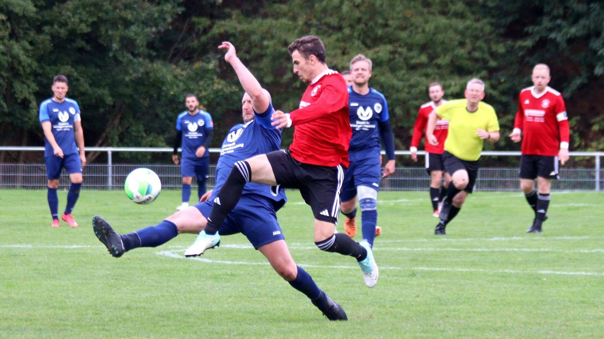 Zweikampf zwischen zwei Fußballern. Einer versucht mit einem Spreizschritt an den Ball zu kommen, der andere verliert die Bodenhaftung.