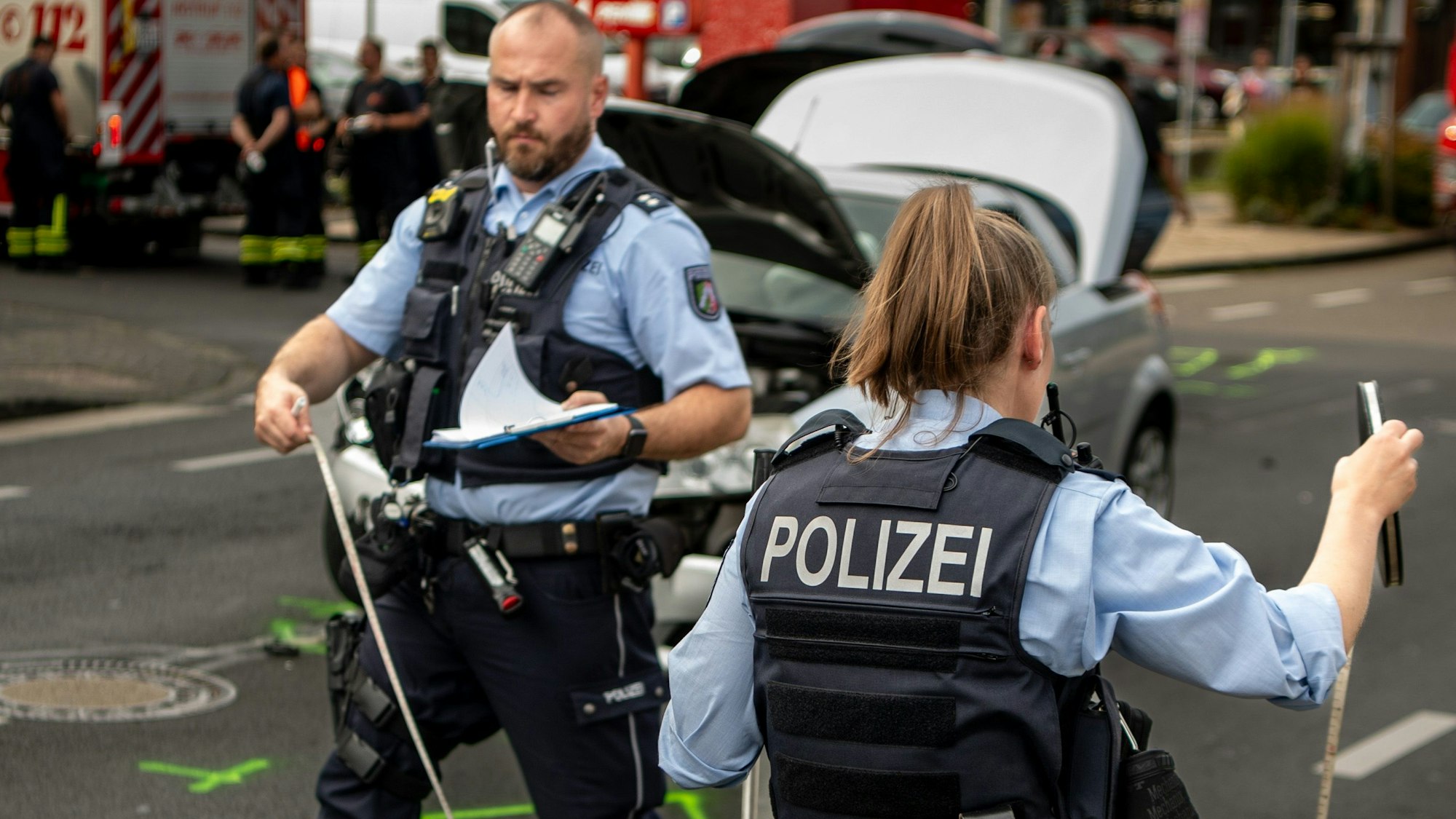 Das Bild zeigt eine Polizistin und einen Polizisten bei der Aufnahme eines Verkehrsunfalls in Euskirchen. Sie haben beide ein Maßband in der Hand.