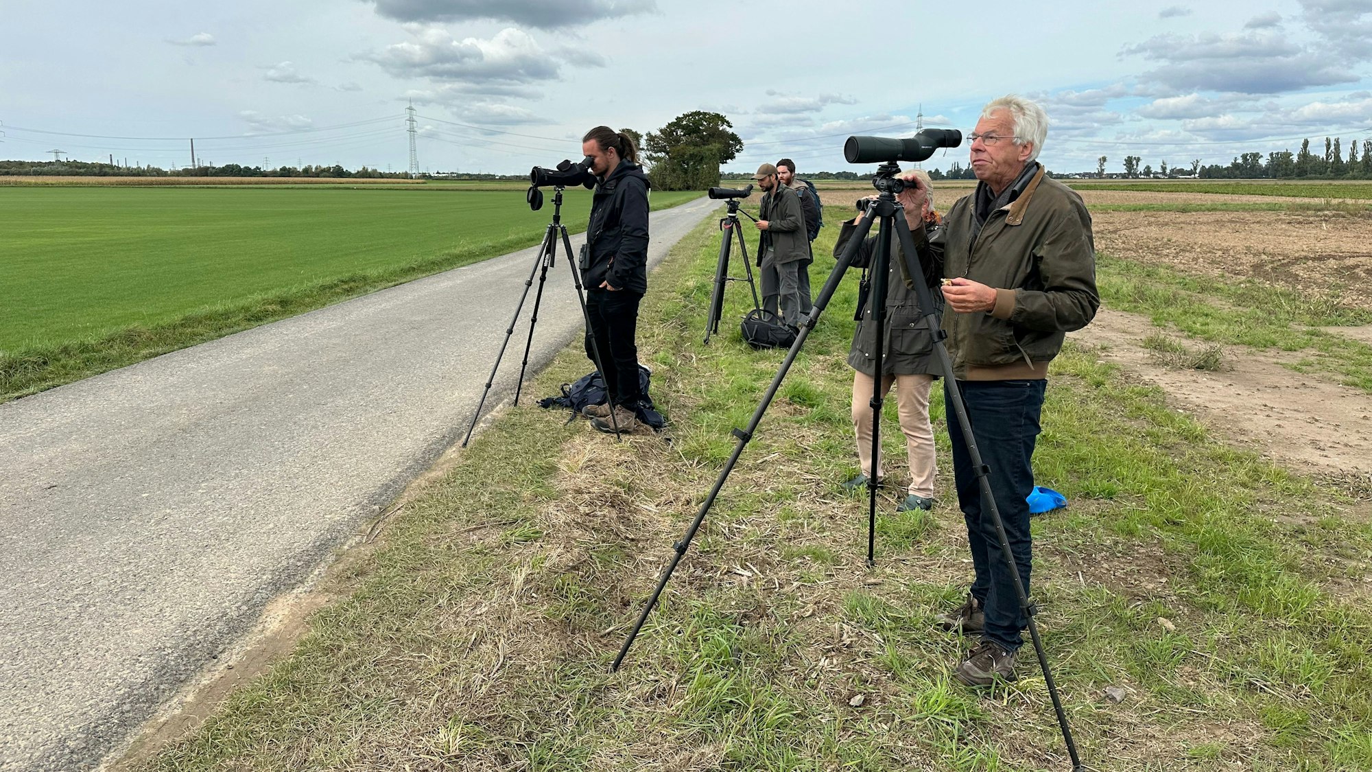 Vogelkundler stehen mit Ferngläsern am Feldrand.