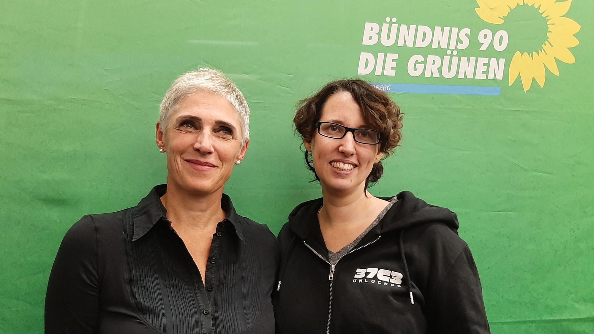 Zwei Frauen vor einem grünen Parteitransparent.