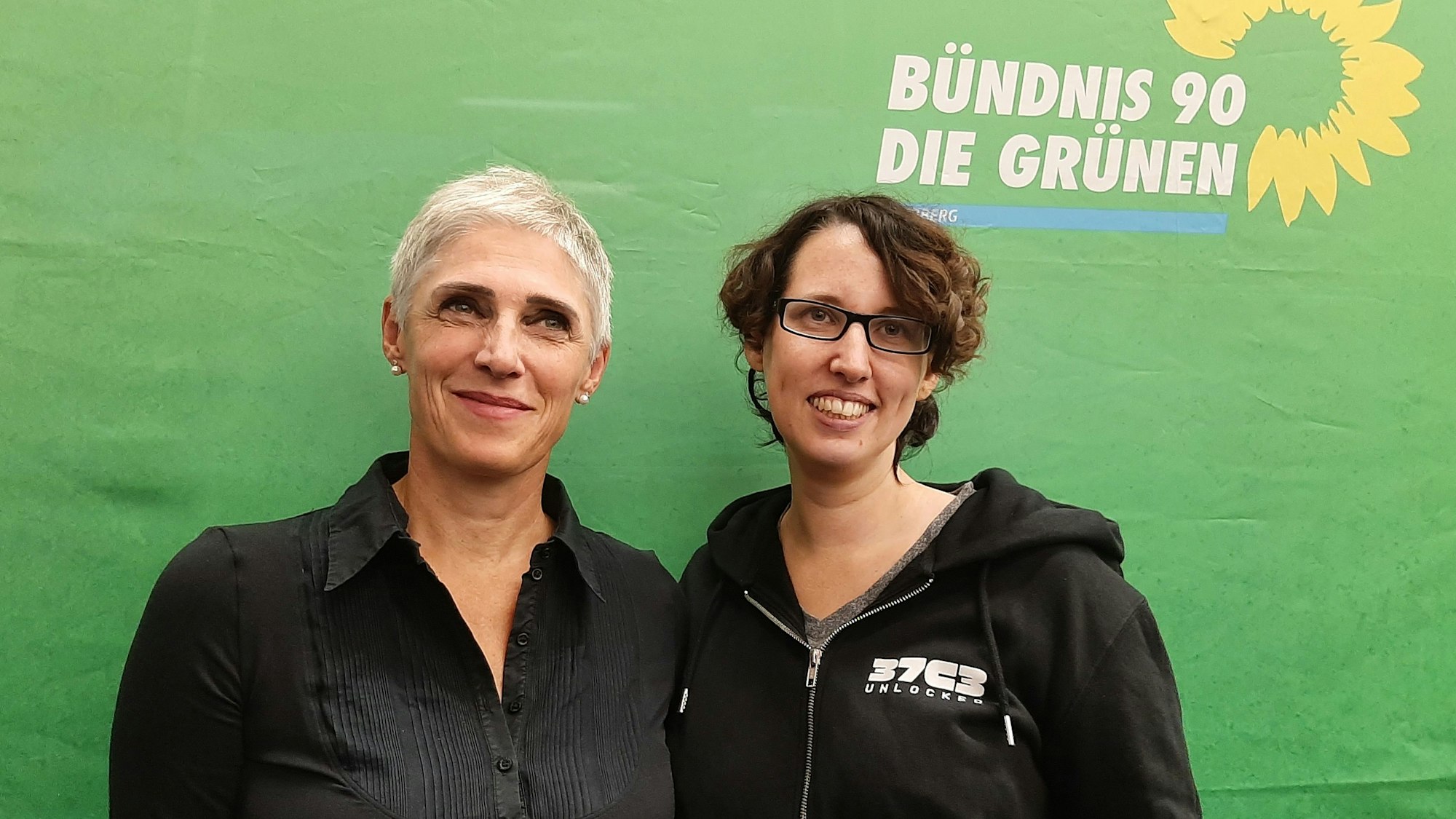 Zwei Frauen vor einem grünen Parteitransparent.