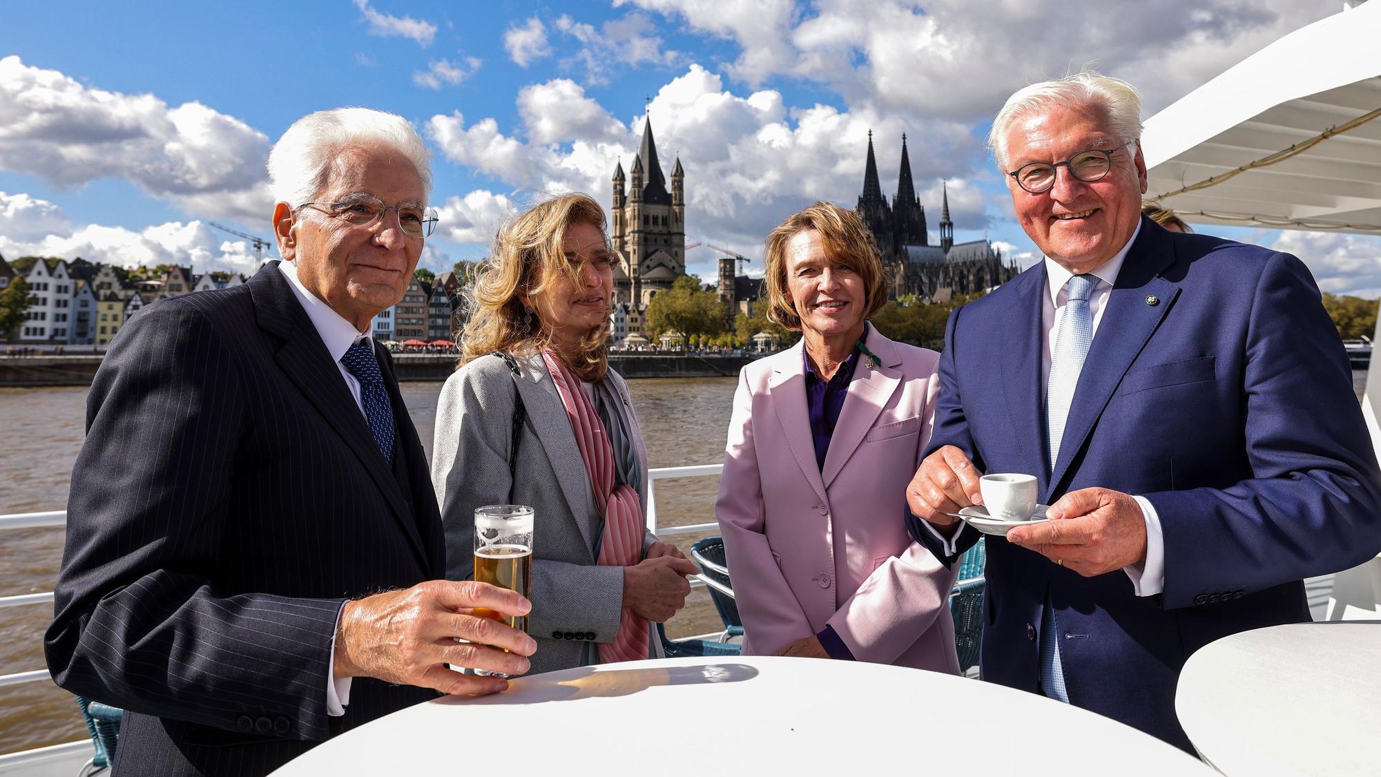 Italiens Präsident Sergio Mattarella (l.), seine Tochter Laura Mattarella (2.v.l.) und Bundespräsident Frank-Walter Steinmeier mit seiner Frau Elke Büdenbender an Bord eines Schiffes, im Hintergrund der Kölner Dom.