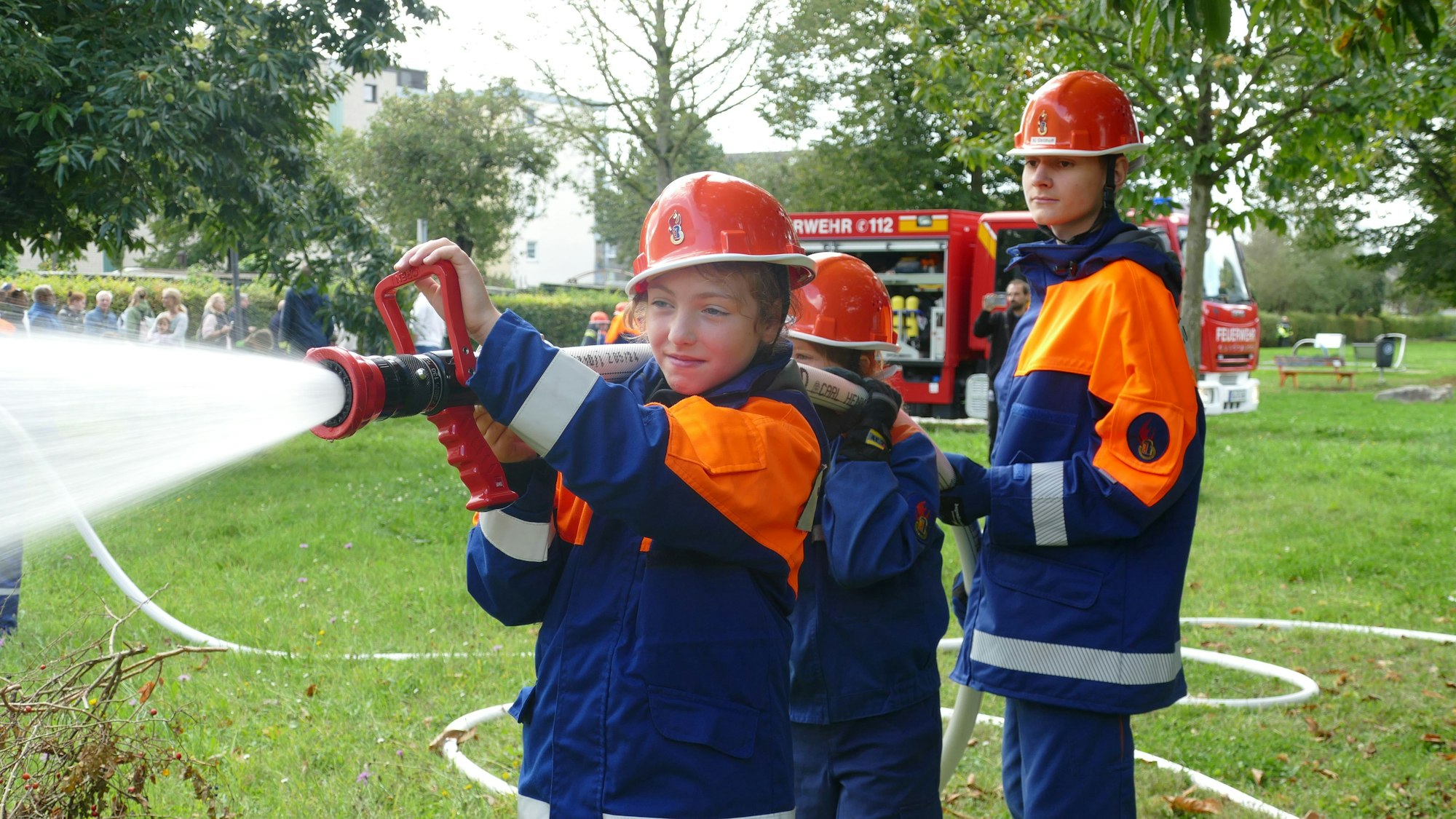 Drei Kinder der Jugendfeuerwehr Tropisdorf-Altenrath spritzen Wasser mit einem Schlauch.