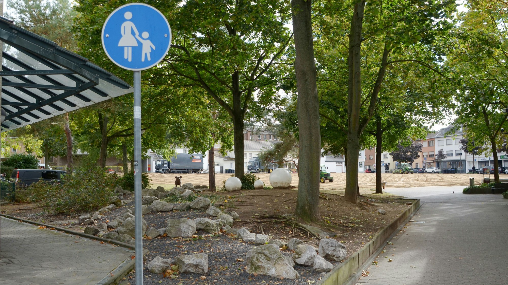 Ein Fußgängerweg führt an einem Hochbeet entlang in die ehemalige Grünanlage, die momentan brachliegt.