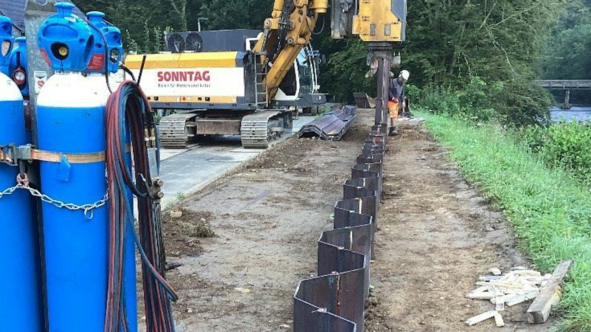 Ein Bagger und ein Bauarbeiter am Flussufer