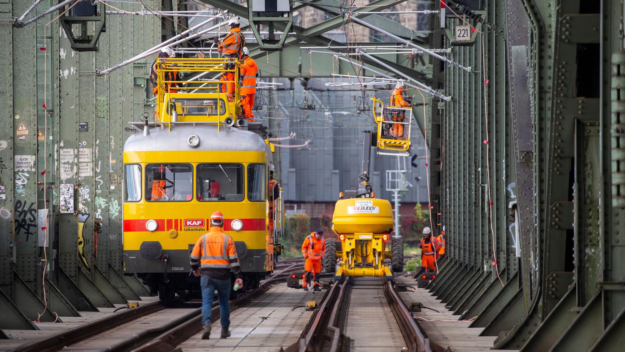 Arbeiter stehen mit Spezialfahrzeugen auf den Schienen und arbeiten an der Oberleitung.