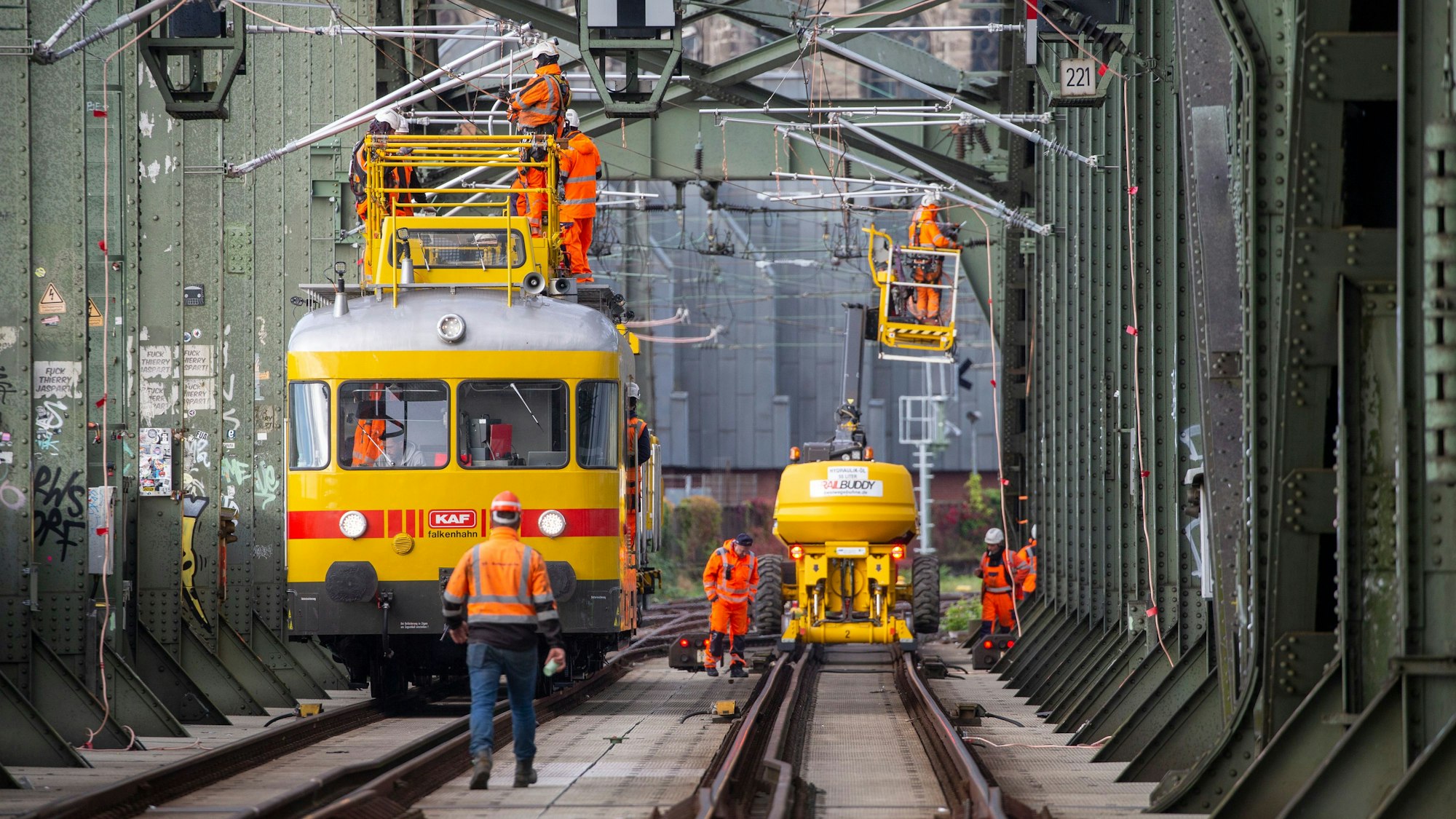Arbeiter stehen mit Spezialfahrzeugen auf den Schienen und arbeiten an der Oberleitung.