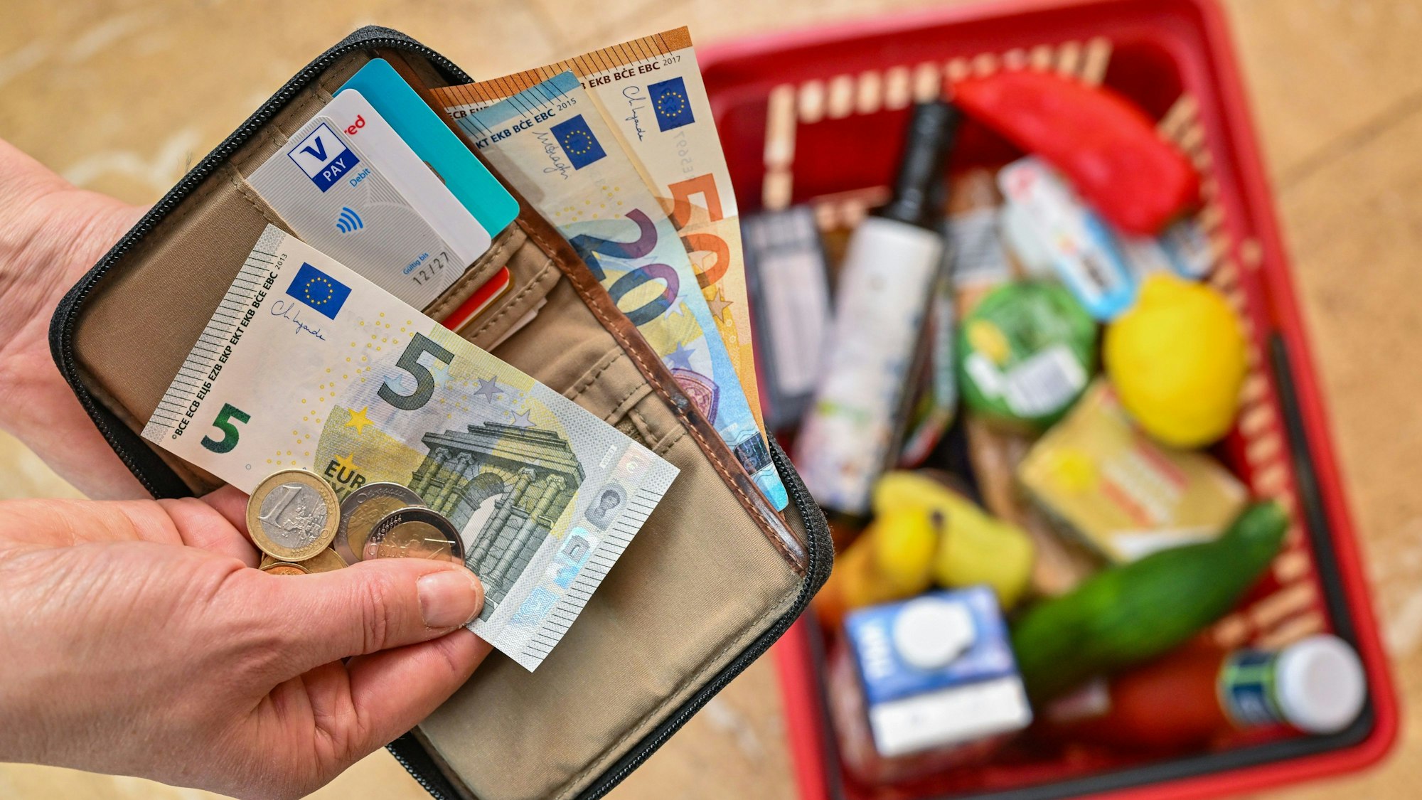 Eine Frau hält auf ihrer Hand Geld vor einem vollen Einkaufskorb mit Lebensmitteln.