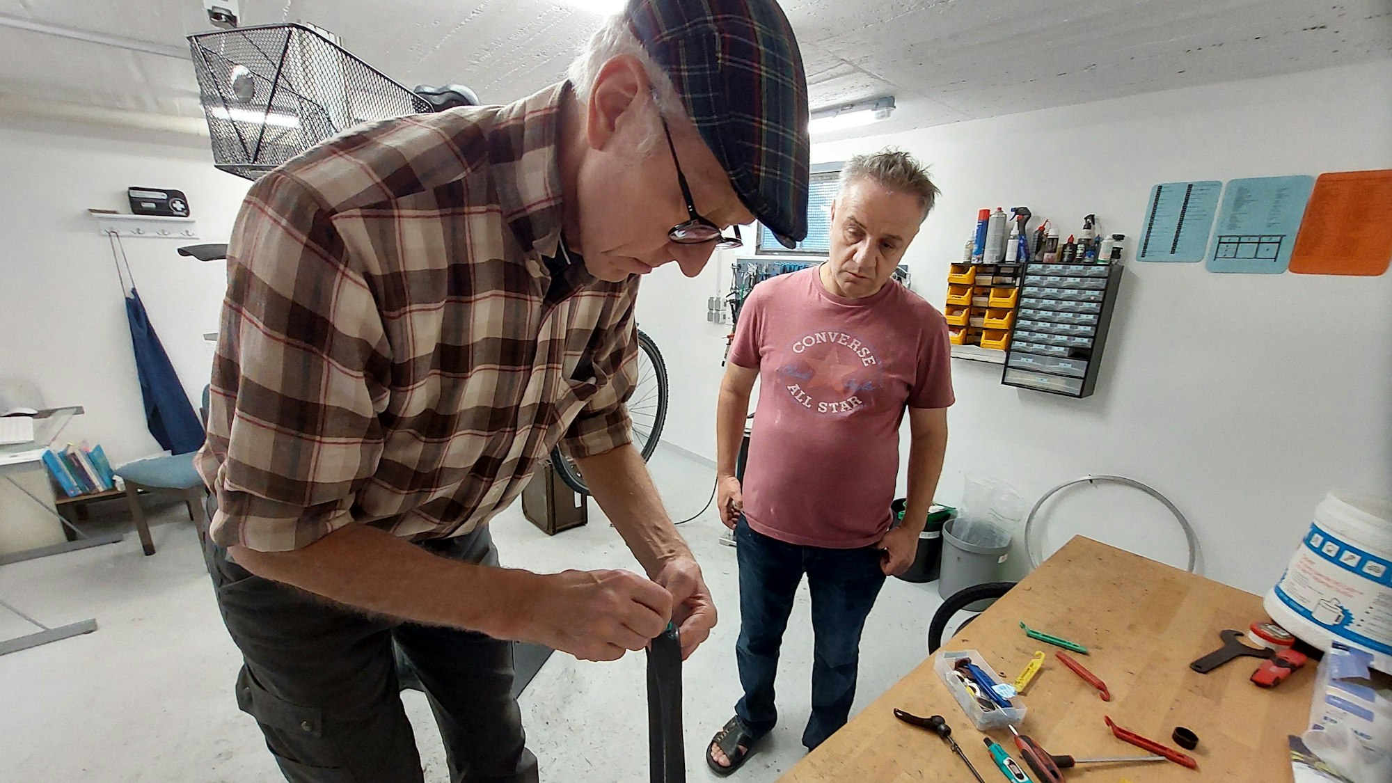 Ein älterer Mann hält einen Fahrradschlauch, ein anderer Mann schaut zu.