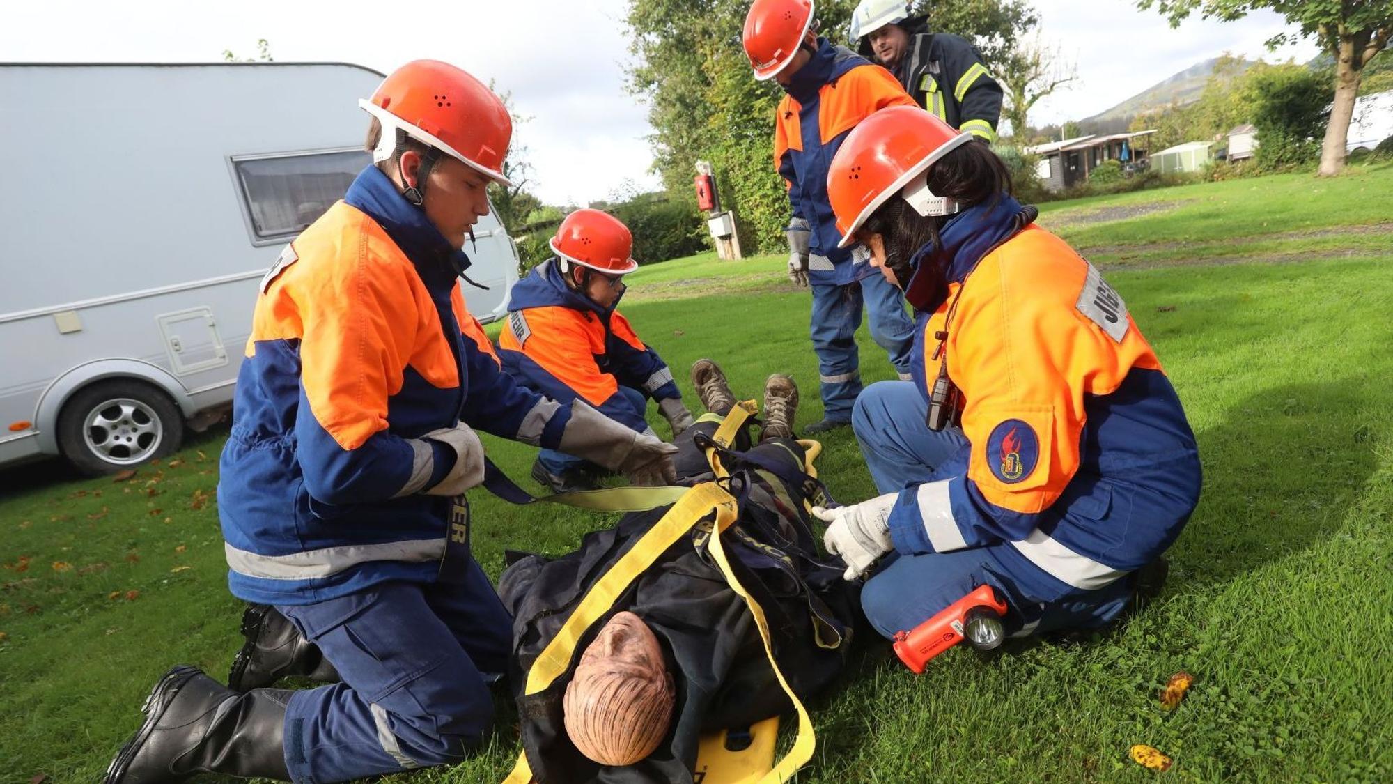 Mitglieder Jugendfeuerwehr spannen Gurte um eine Puppe, die auf einer Trage liegt.