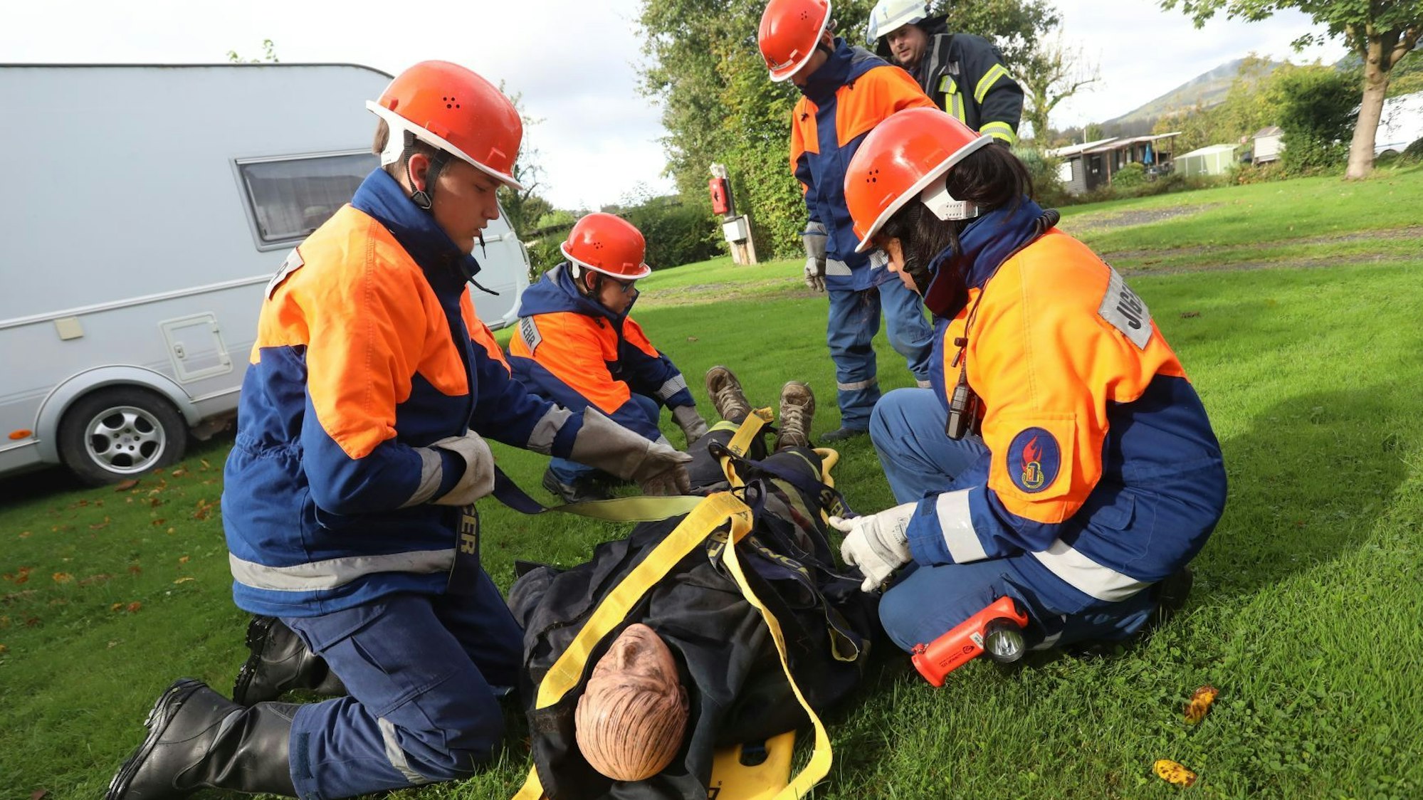 Mitglieder Jugendfeuerwehr spannen Gurte um eine Puppe, die auf einer Trage liegt.