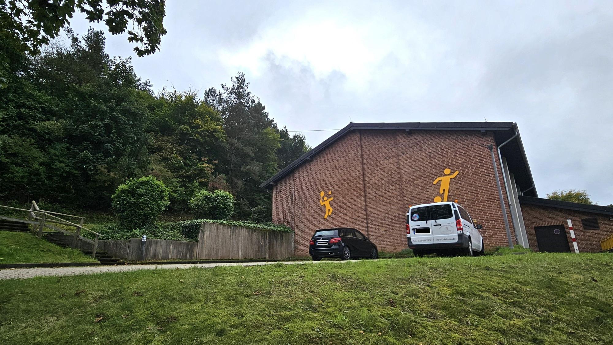 Blick auf die Turnhalle und die Bäume, die im Hang darüber stehen.
