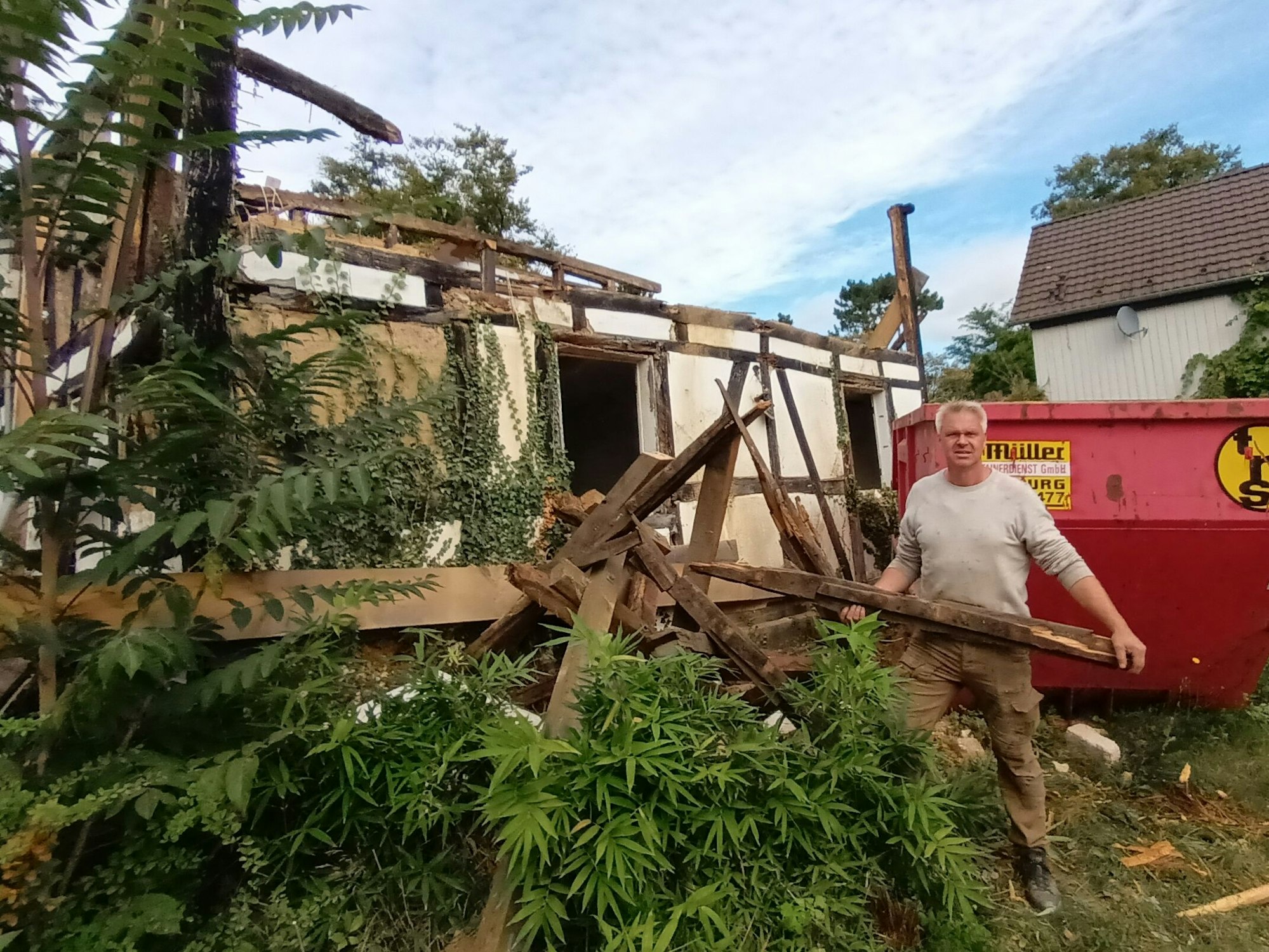 Ein Mann steht mit einem Balken vor einem Abbruchhaus
