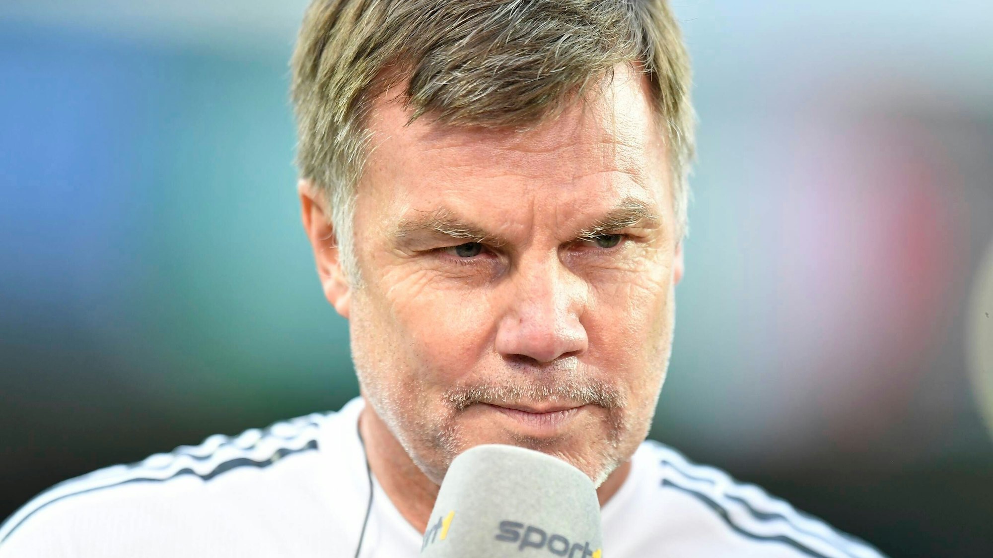 Das Foto zeigt Thomas Helmer im Trikot hinter einem Mikrofon.