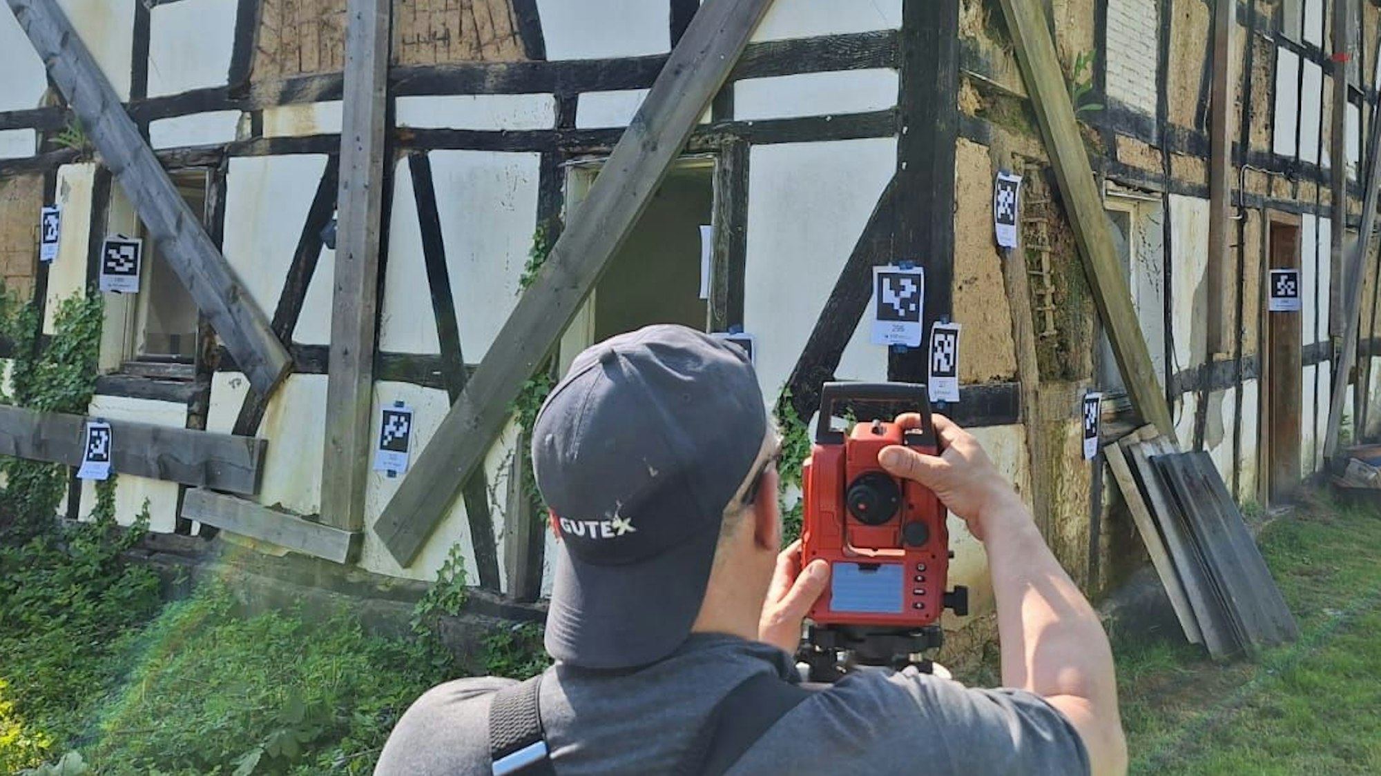Ein Mann filmt ein baufälliges Fachwerkhaus, an dem Markierungen angebracht sind.