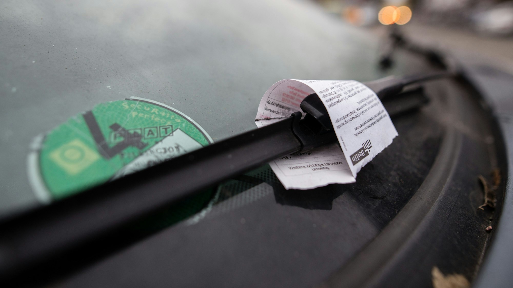 Ein Strafzettel hängt an einer Windschutzscheibe.