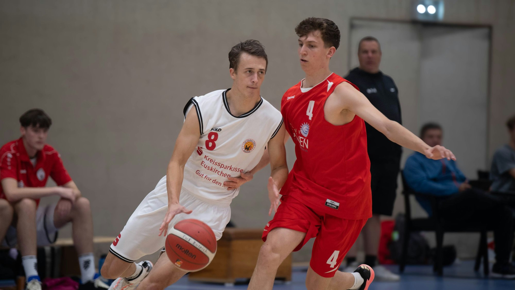 Ein Spieler in einem weißen Trikot führt den Ball, sein Kontrahent (in Rot) bedrängt ihn.