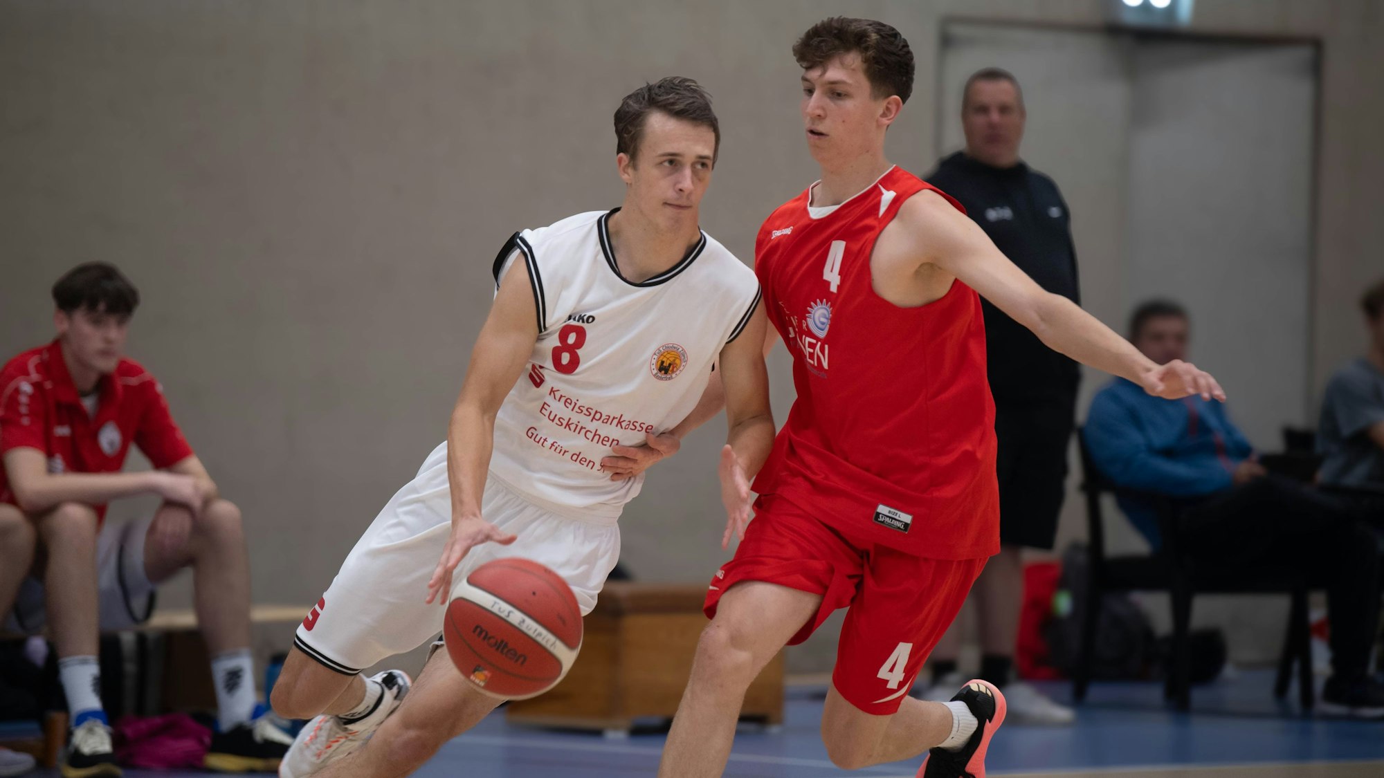 Ein Basketballer des TuS Zülpich im weißen Trikot dribbelt den Ball an seinem Kontrahenten von den Erftbaskets vorbei.