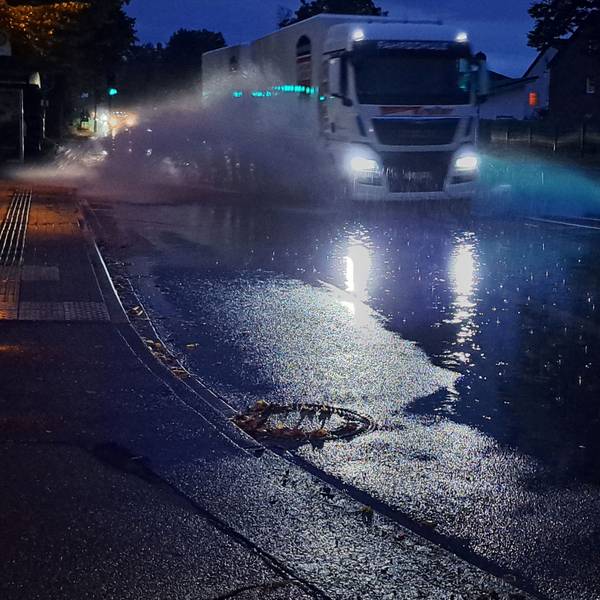 Ein Lkw fährt durch eine große Pfütze und Wasser spritzt hoch.