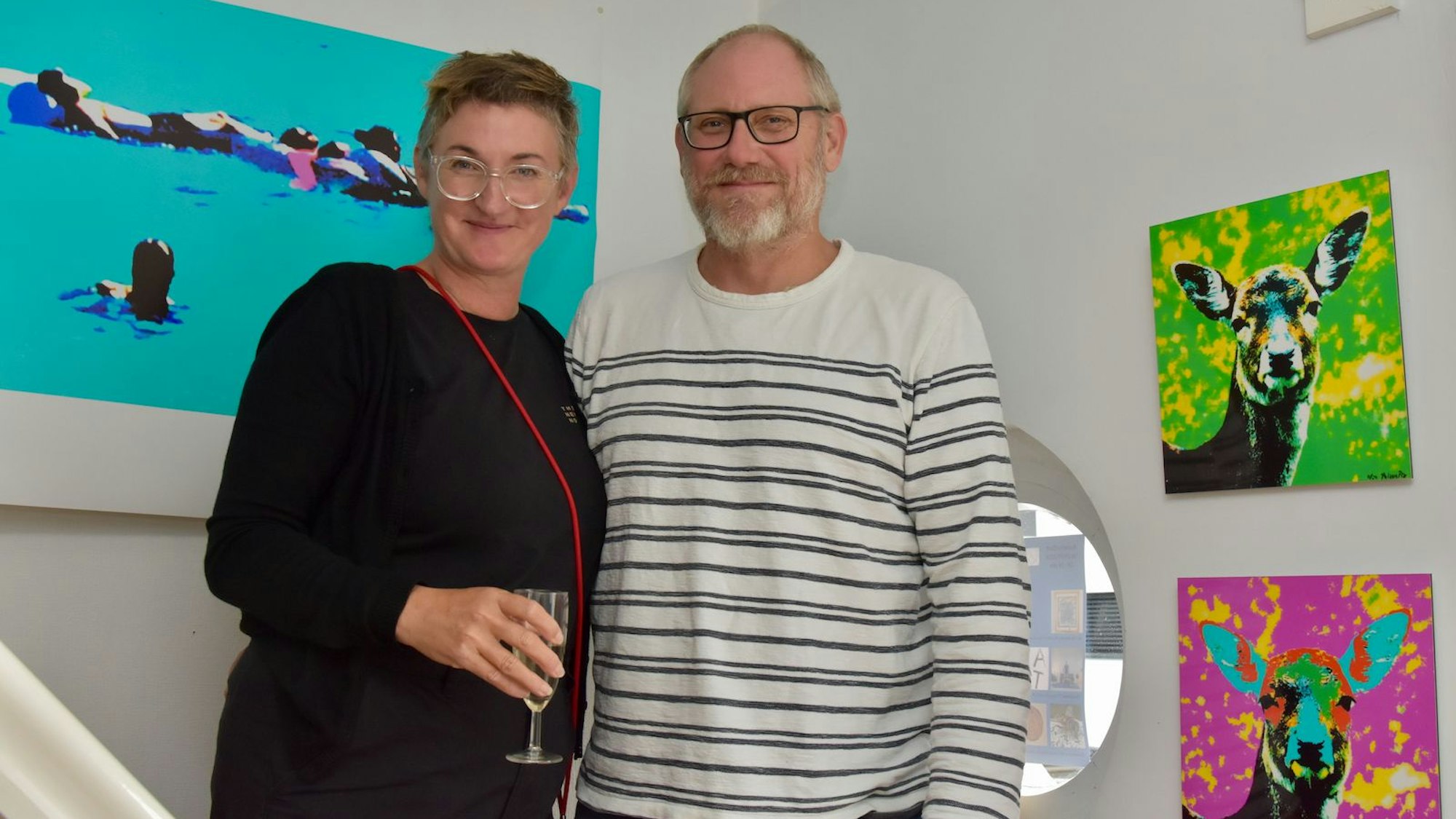 Eine Frau und ein Mann stehen vor bunten Bildern.