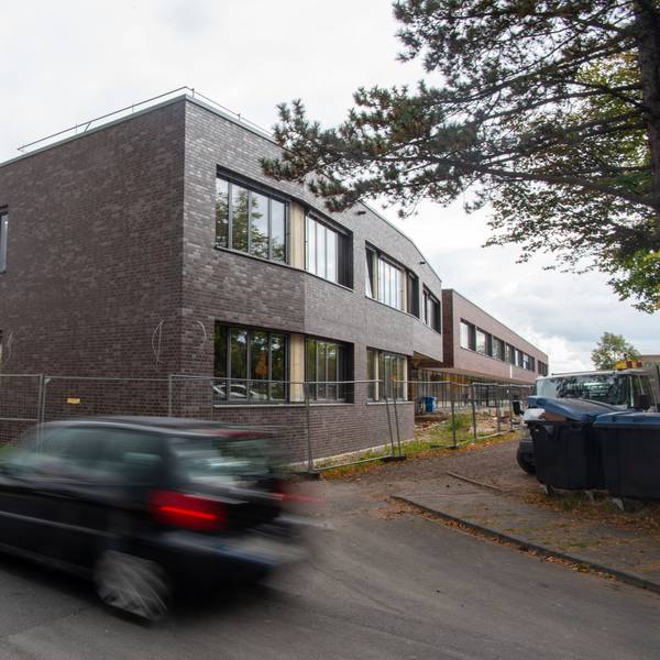Ein Auto fährt an dem fast fertigen Erweiterungsbau am Schulcampus Zülpich vorbei. Das Gebäude steht hinter einem Bauzaun, rechts im Bild sind Mülltonnen zu erkennen.