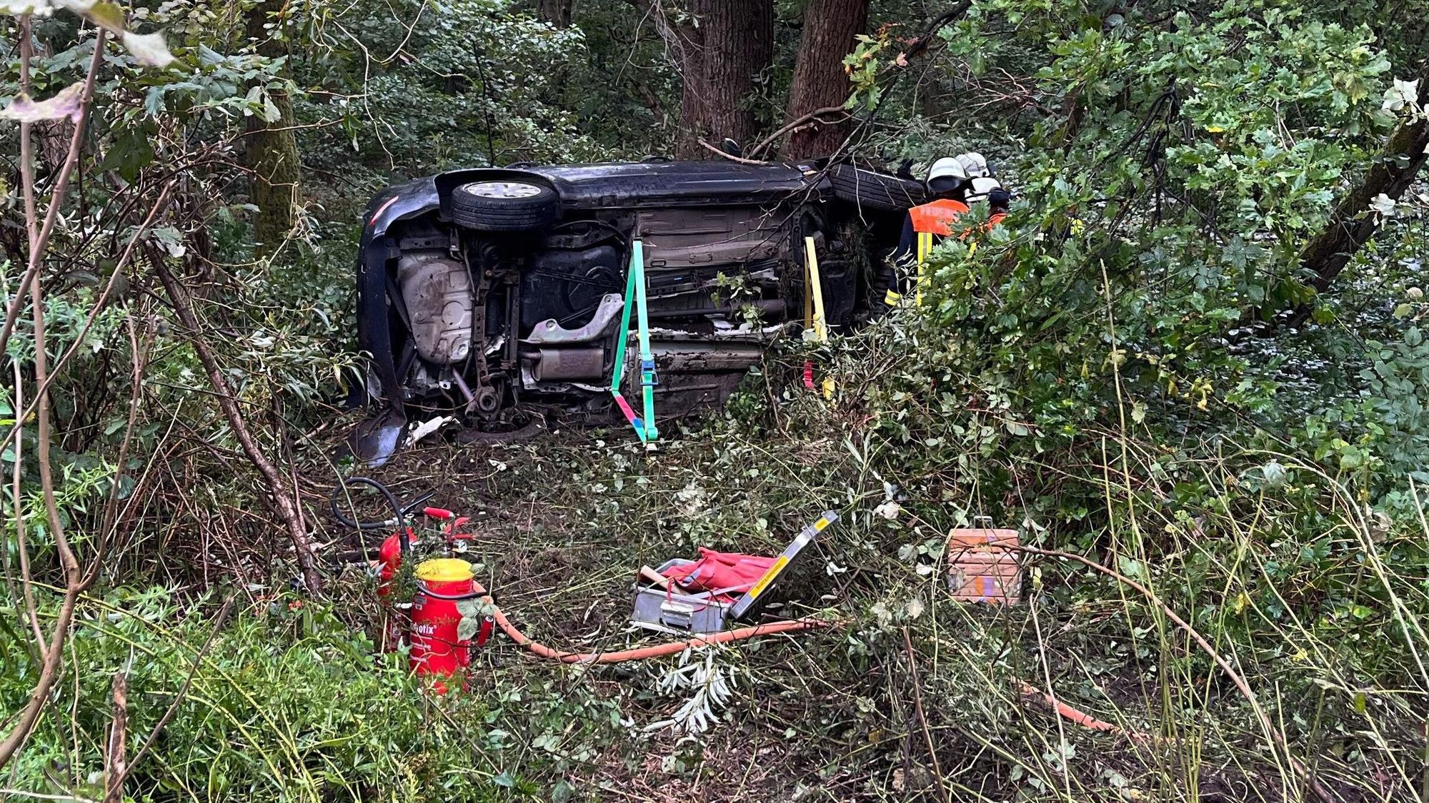 Ein Pkw überschlug sich mehrfach und blieb auf der Seite liegen. Feuerwehrleute sichern das Fahrzeug.