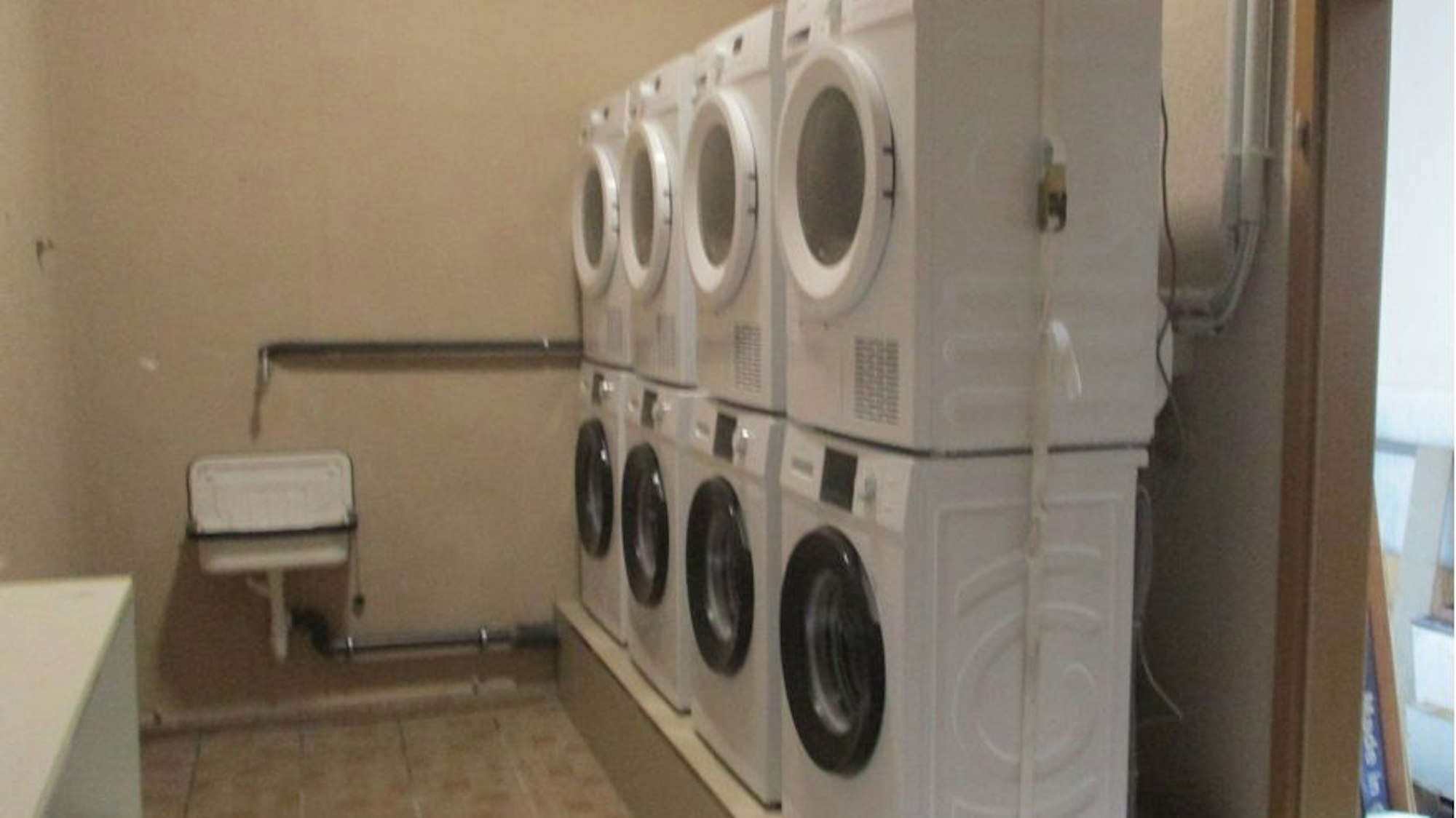 Vier Waschmaschinen und vier darauf stehende Wäschetrockner, daneben ein Handwaschbecken.