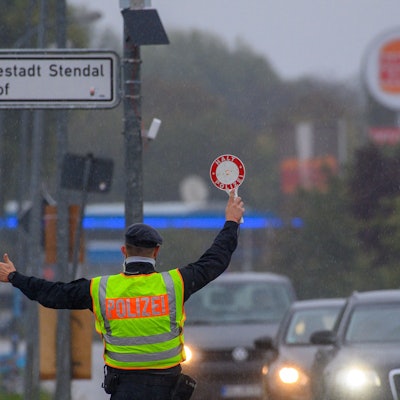 Ein Polizist winkt mit einer Polizeikelle einen Autofahrer aus dem Straßenverkehr.