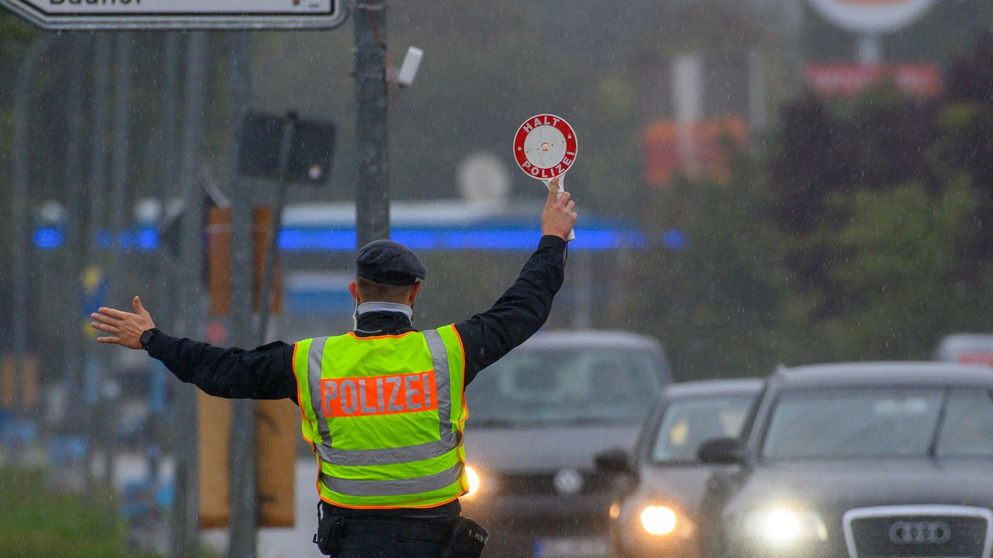 Ein Polizist winkt mit einer Polizeikelle einen Autofahrer aus dem Straßenverkehr.
