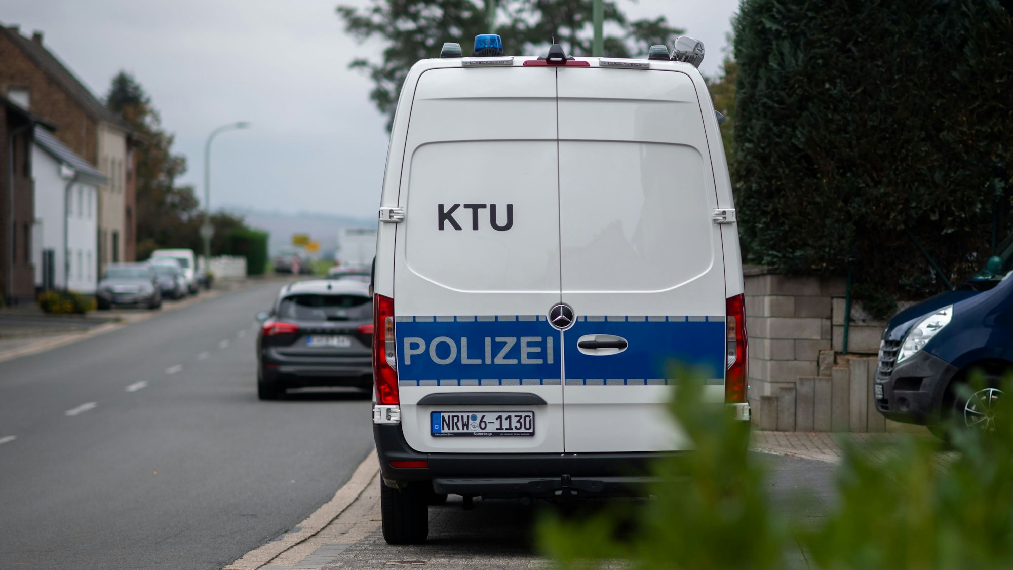 Das Bild zeigt ein Fahrzeug der Polizei, das in einem Dorf am Straßenrand steht. Im Hintergrund sind andere Autos zu erkennen.