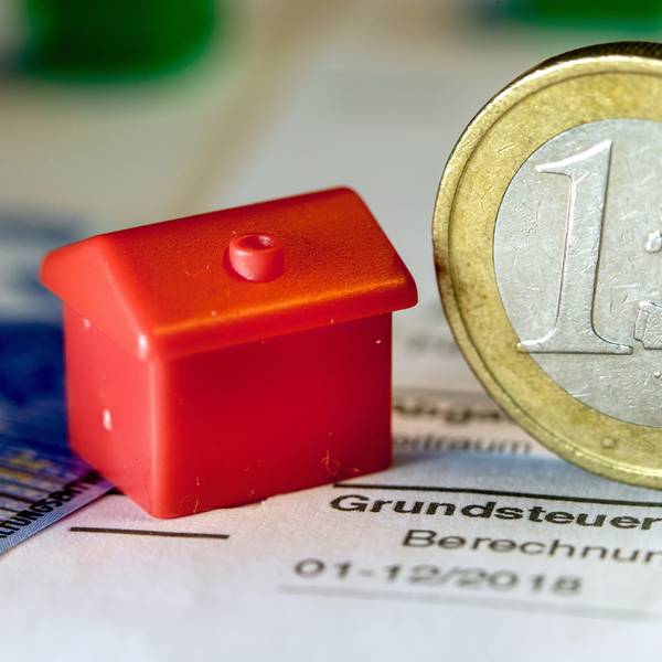 Eine Euro-Geldmünze sowie ein Spielzeughaus stehen auf einem Abgabenbescheid für die Entrichtung der Grundsteuer.