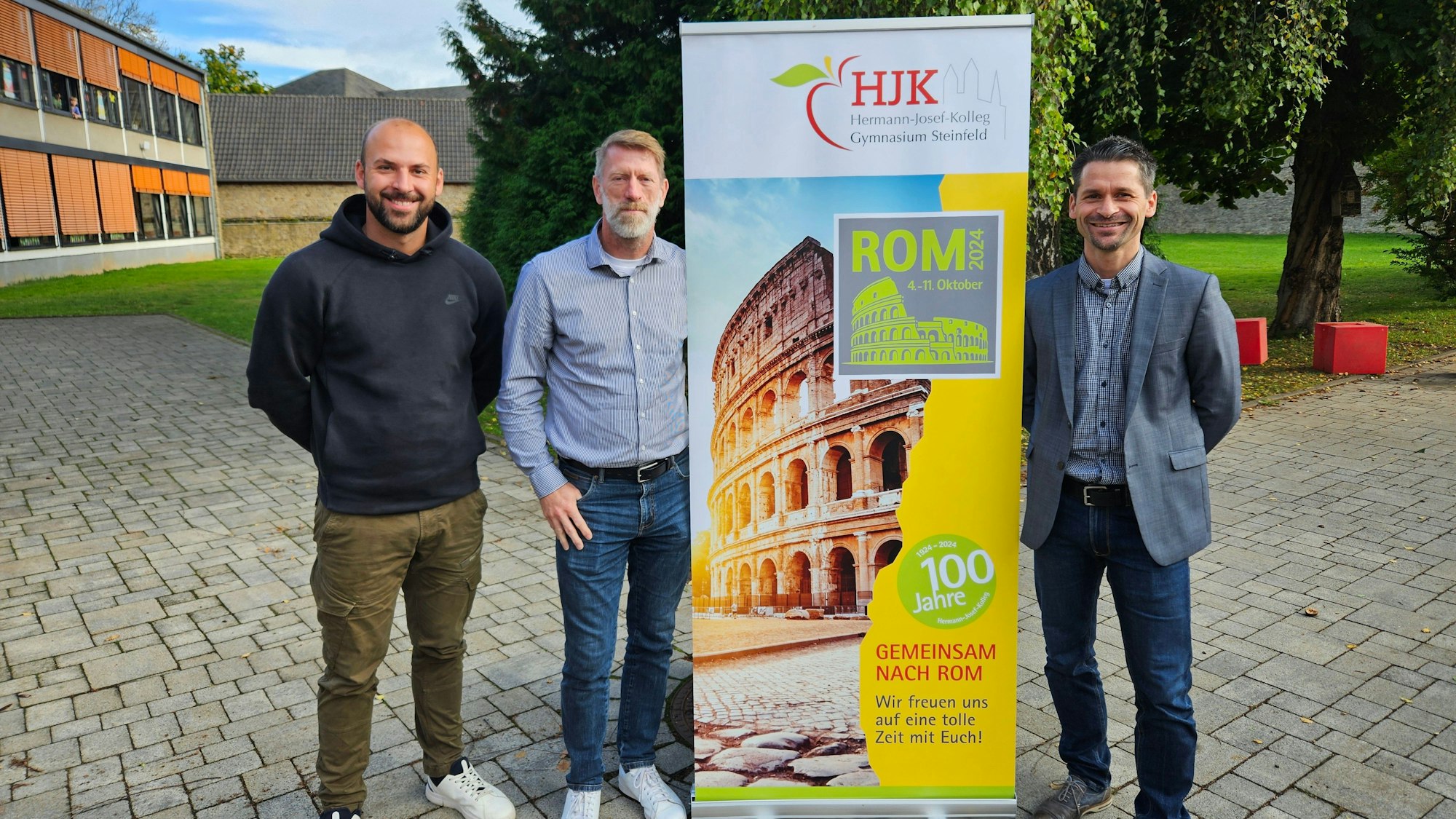 Andreas Winkler, Ralf Kremp und Thomas Frauenkron stehen neben einem Aufsteller, der für die Romfahrt wirbt.