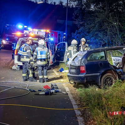 Feuerwehrleute stehen mit Rettungsgerät vor einem Unfallauto.