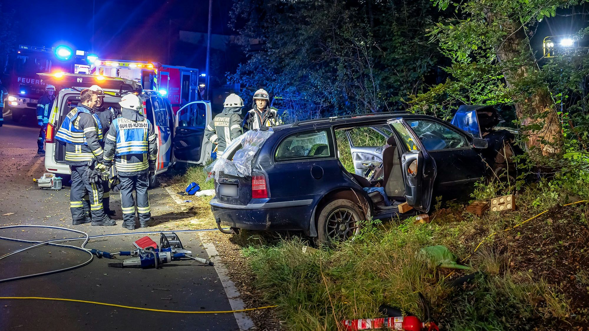 Feuerwehrleute stehen mit Rettungsgerät vor einem Unfallauto.