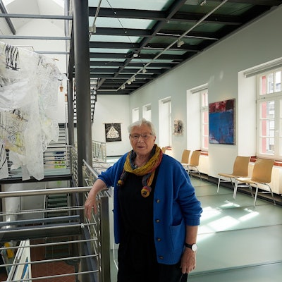 Kuratorin Eva-Maria Hermanns steht im Kunstforum in Gemünd an einer Arbeit von Helga Mols, die im Treppenaufgang installiert ist.